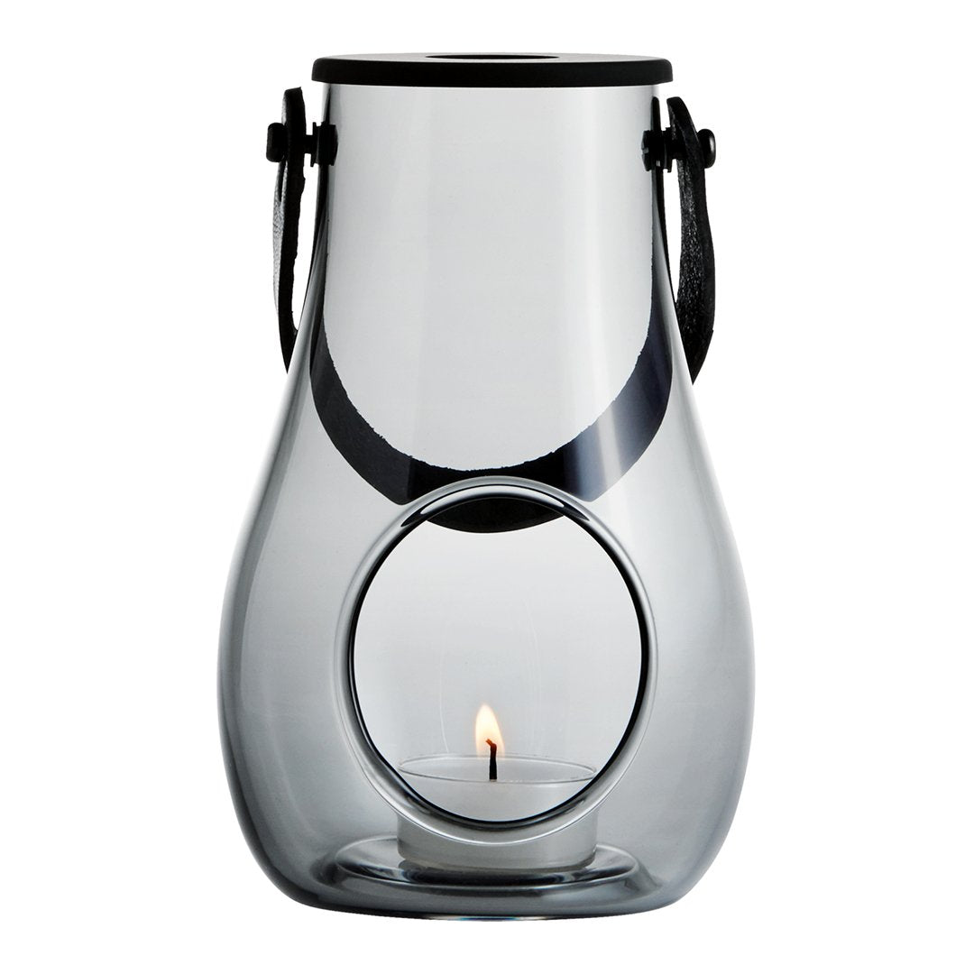 Clear glass lantern with a sleek black handle and circular cutout, showcasing a warm candlelight glow.