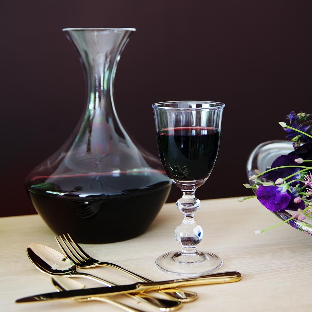 Elegant wine decanter and vintage glass, showcasing deep red hues against a dark backdrop. Gold-tinted cutlery accents.