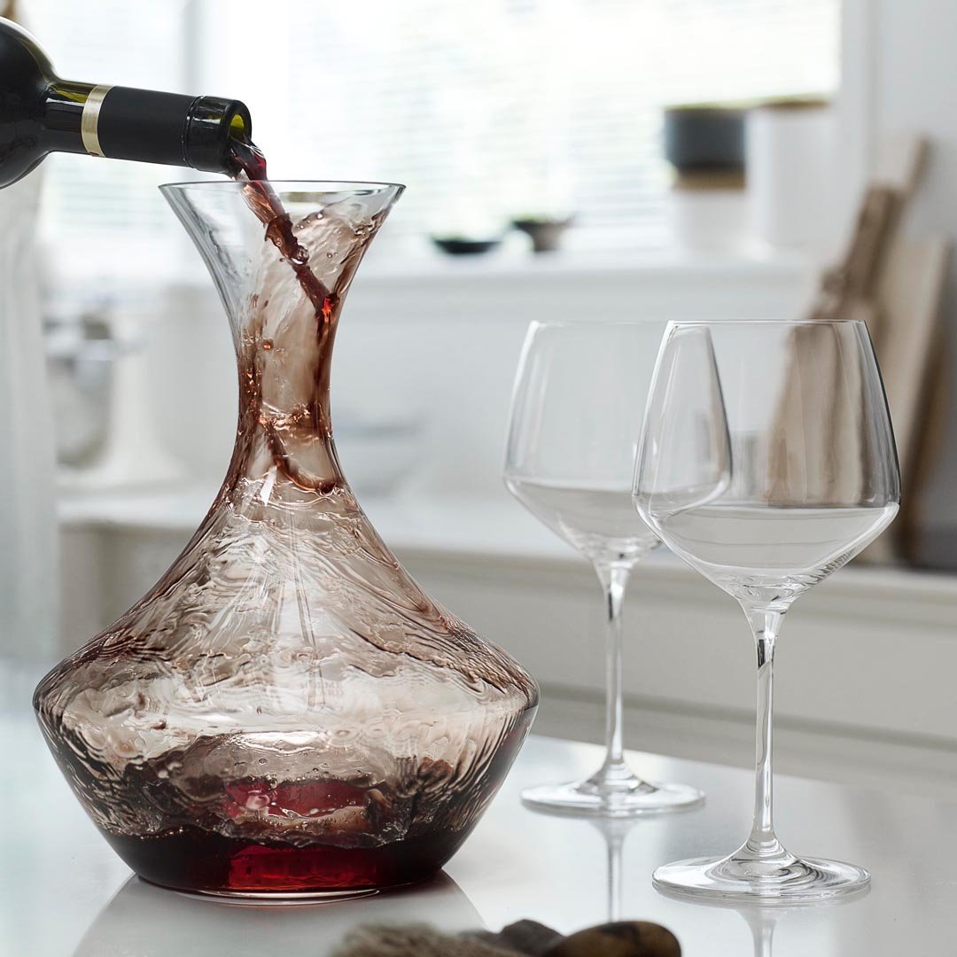 Artisan red glass wine decanter with intricate swirls, accompanied by elegant clear crystal wine glasses.