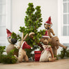 "Wooden animal figurines with red hats and natural tones, surrounded by green foliage and festive decor."