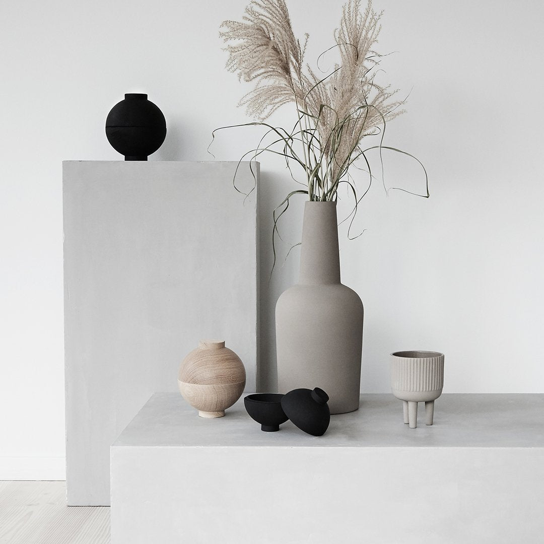 "Neutral-toned vases and decor with textures, featuring black, grey, and earthy shades on minimalist surfaces."