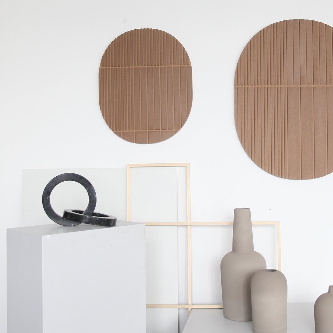 "Brown textured wall decor in oval shapes with minimalist gray and black vases on a sleek white display."