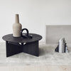 Round black coffee table with a textured wood finish, paired with a neutral beige vase and contrasting black accents.