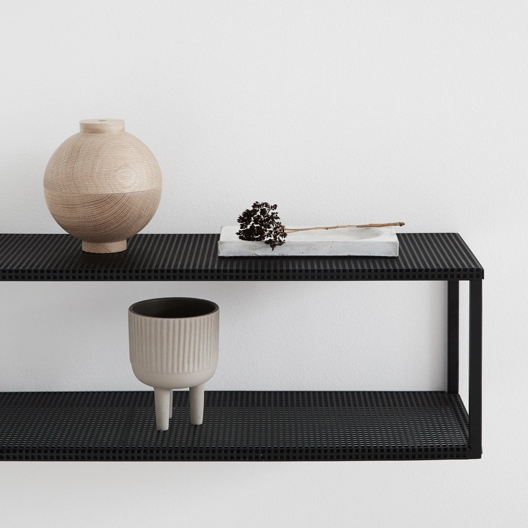 Black textured shelf with a wooden vase, gray ceramic pot, and minimal decor items in neutral tones.