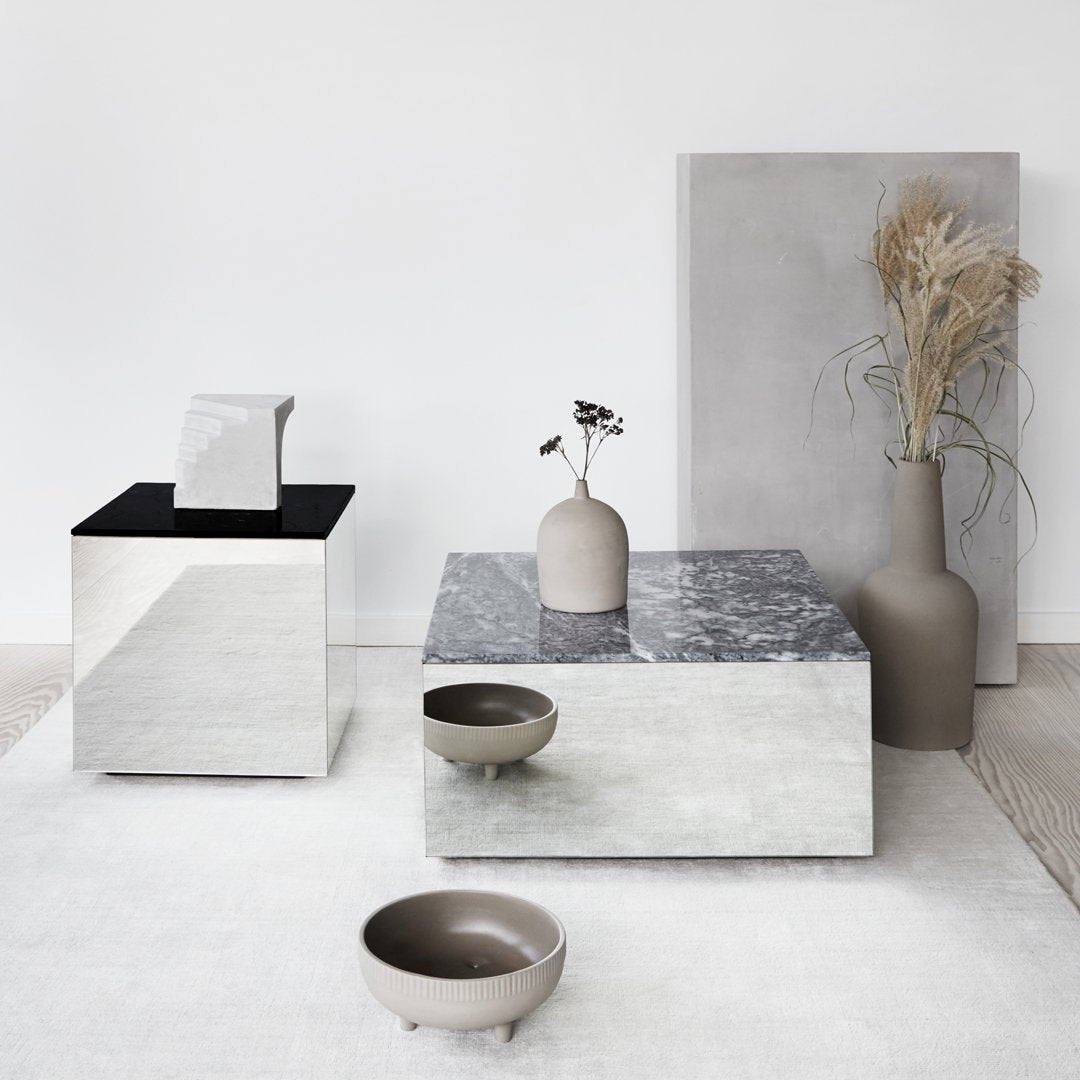 Elegant gray and black tables with smooth surfaces, complemented by neutral vases and earthy tones in a minimalist setting.