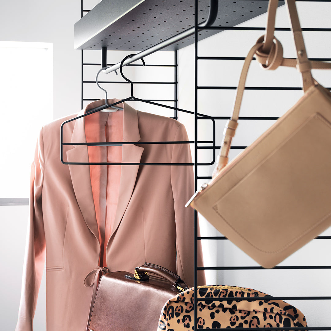Pink blazer, neutral tan bag, and leopard print purse hang on a sleek black rack, vibrant and stylish.