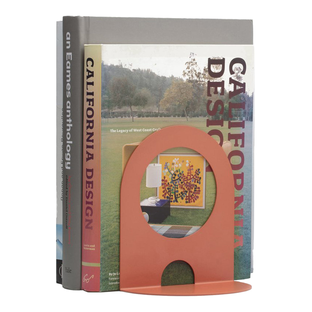 Orange bookend with a modern cutout design, complementing colorful book spines with geometric patterns.