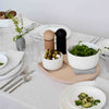 "Modern table setting with white bowls, wood accents, and a neutral tablecloth showcasing greens and sleek minimalist design."