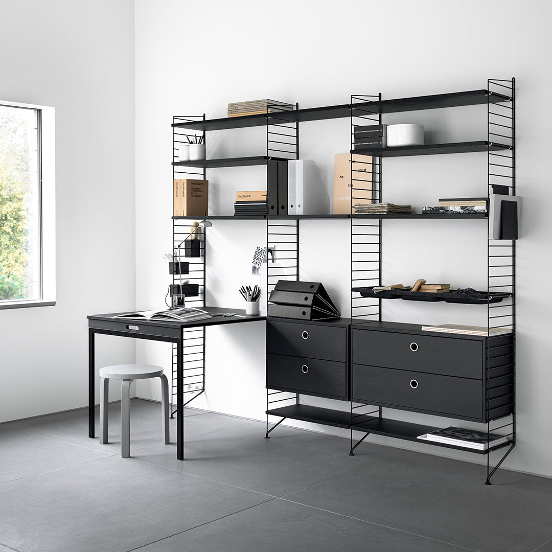 Black metal shelving unit against a white wall, with a matching black desk and gray floor, featuring minimalist design.