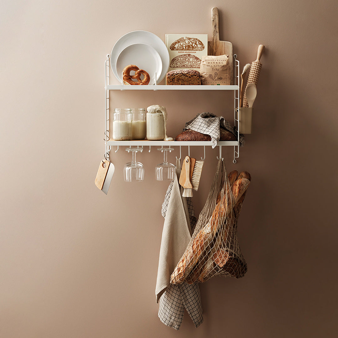 White shelving unit displaying neutral tones and organic textures, featuring woven bags and ceramic dishware.