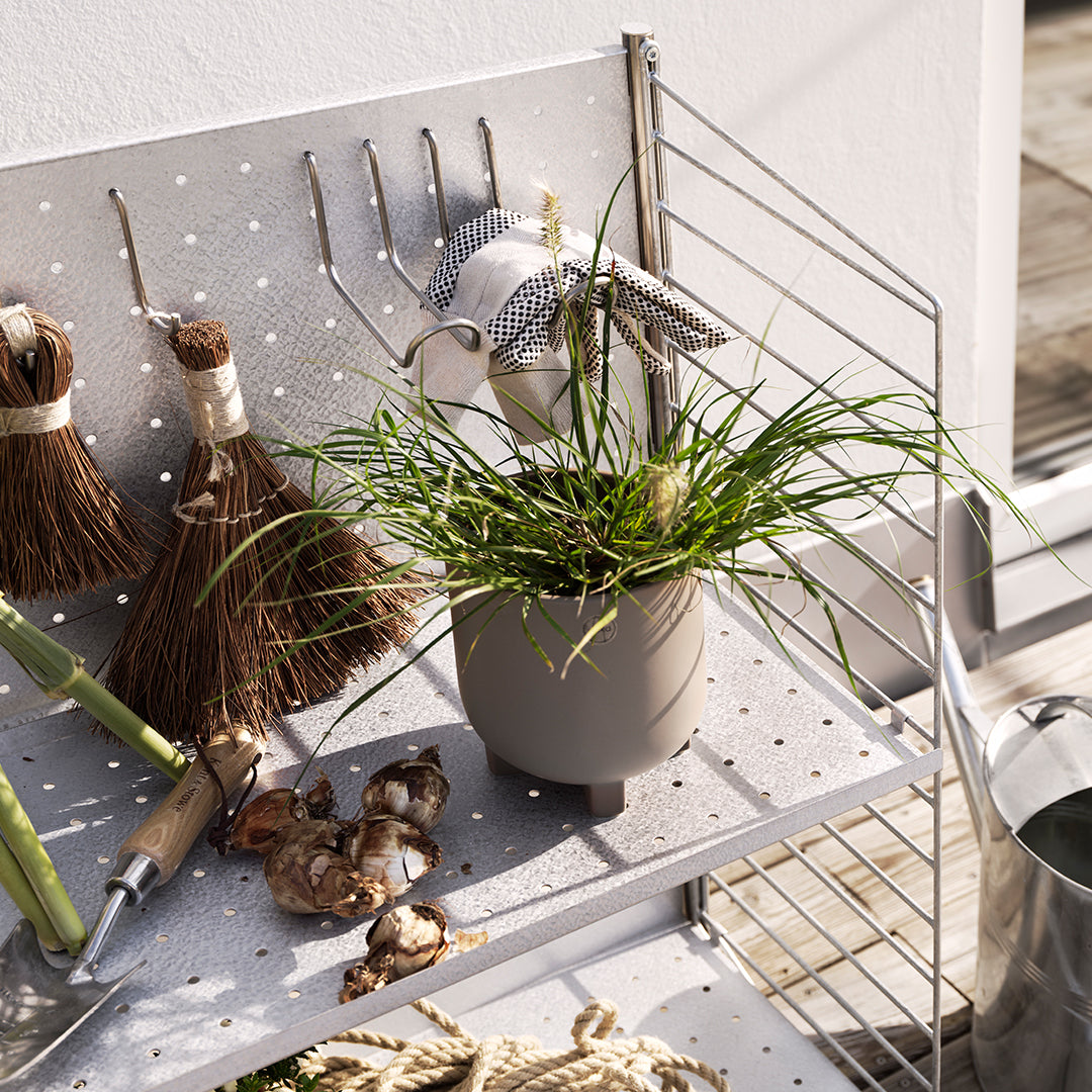 "Gray planter with vibrant green grass on a light pegboard shelf, surrounded by rustic gardening tools."