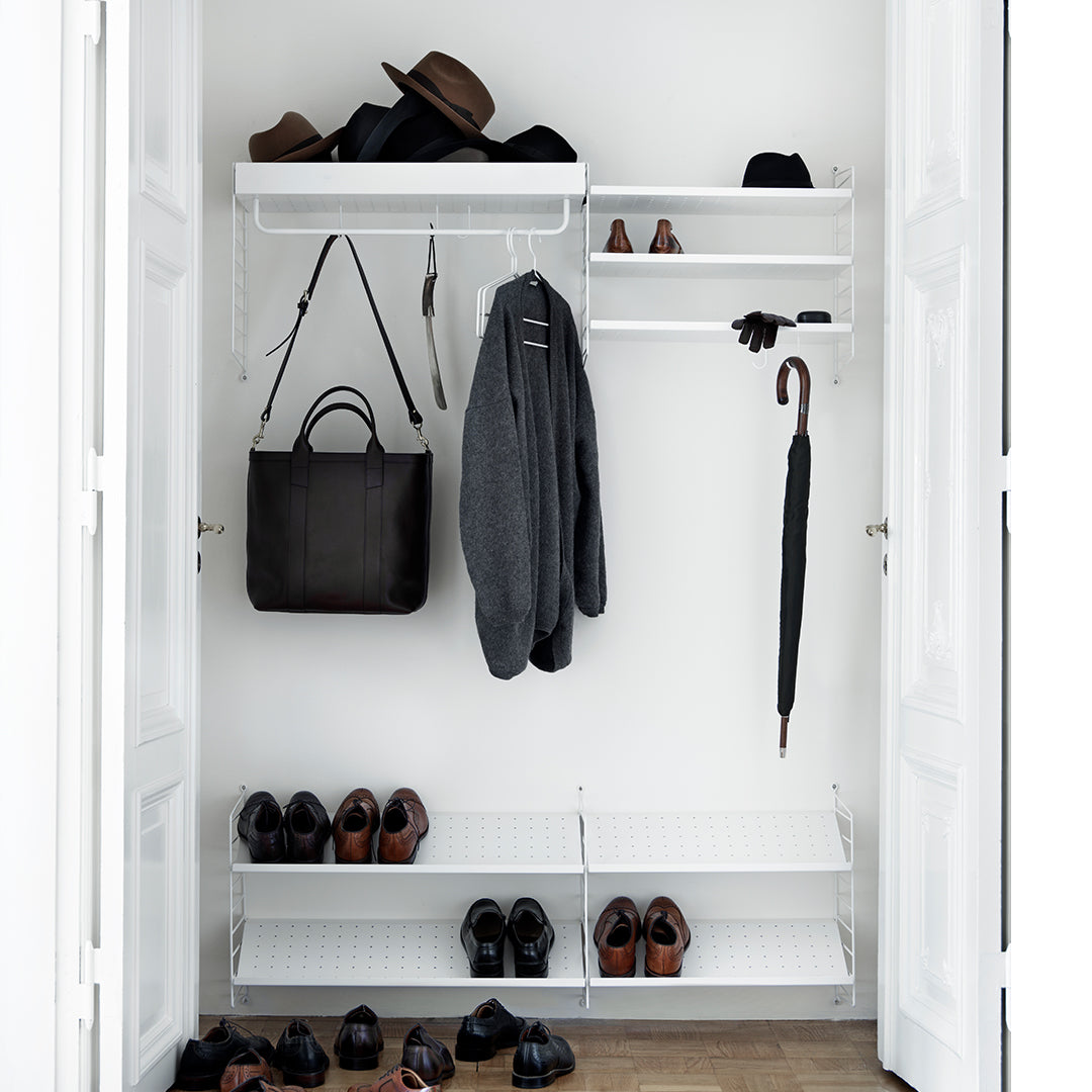 Stylish white closet with black shoes, hats, and a gray coat; sleek and modern design with clean lines.