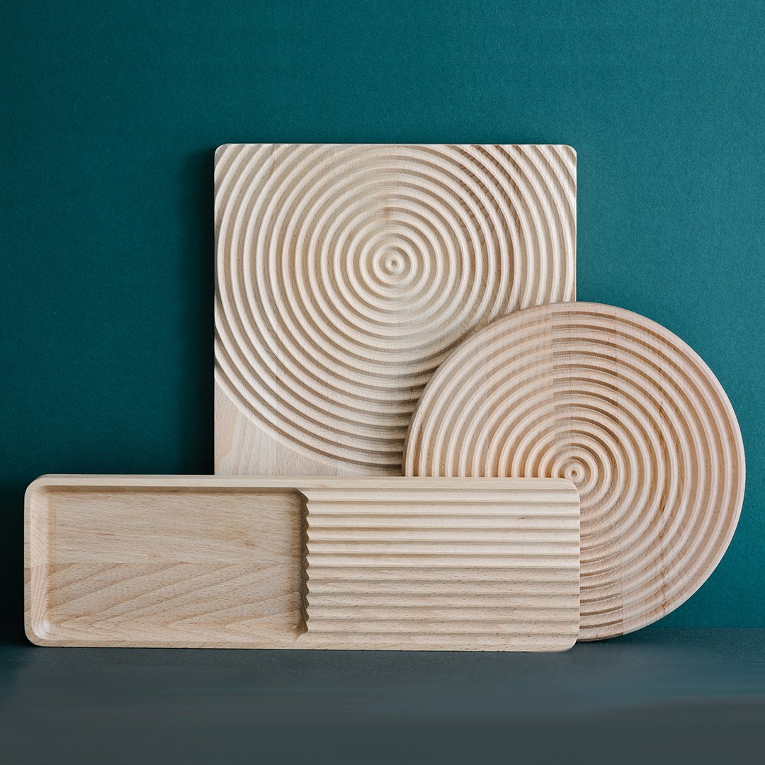 "Three wooden serving trays with circular and linear patterns in natural light wood against a teal background."