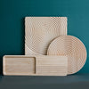 "Three wooden serving trays with circular and linear patterns in natural light wood against a teal background."