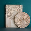 Natural wood serving set featuring a circular ripple pattern on a round plate and rectangular board, against a teal backdrop.