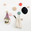 Colorful wall hooks in pastel pink, green, and orange, paired with a black hat and a textured mesh bag.