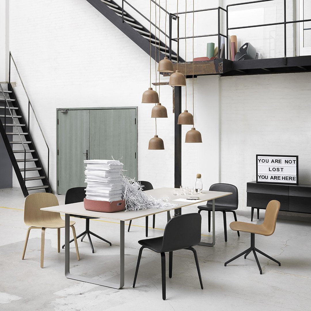 Modern dining room with black and beige chairs, white table, and brown pendant lights against a minimalist backdrop.
