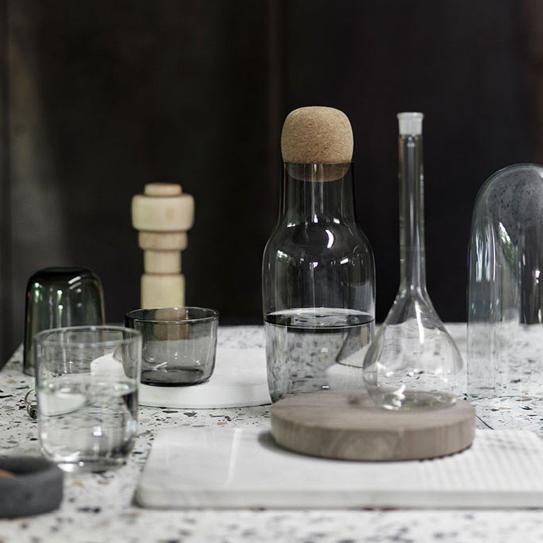 Clear glass bottles and textured wooden elements on a speckled white surface, showcasing modern minimalist design.