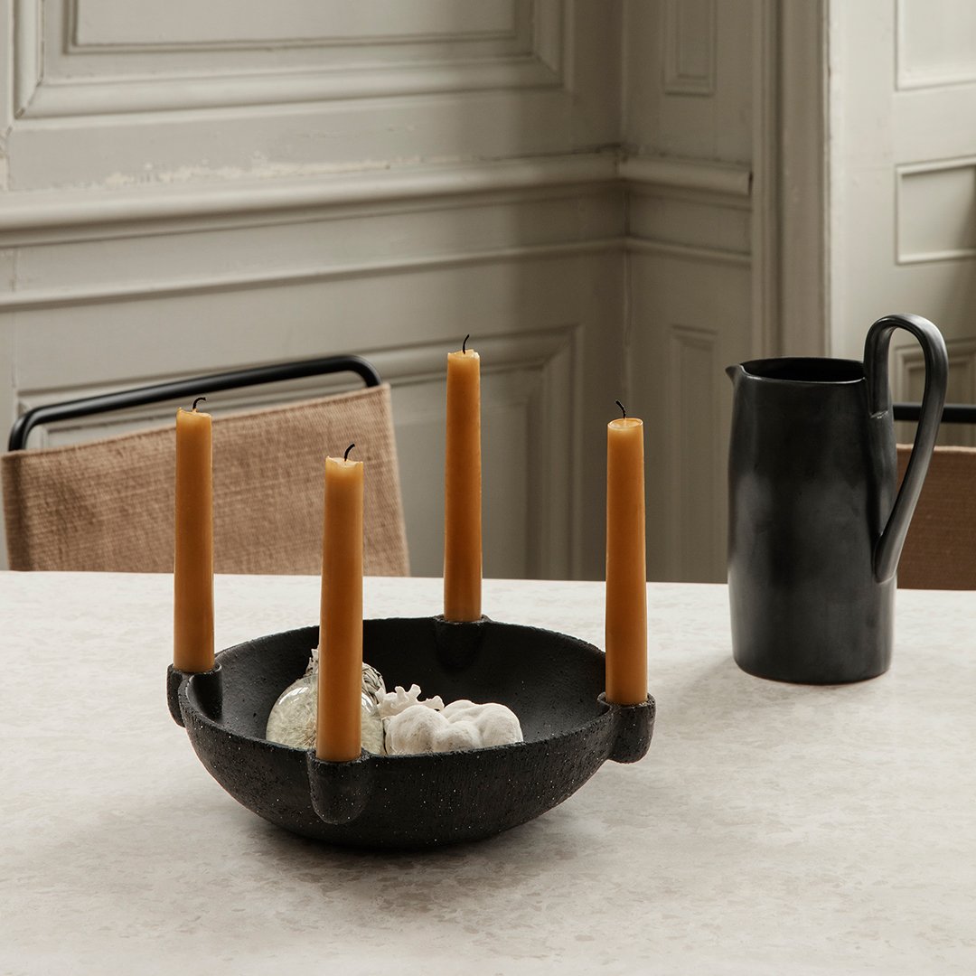 Black bowl with four amber candles and a black pitcher against a neutral textured table surface.