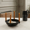 Black bowl with four amber candles and a black pitcher against a neutral textured table surface.