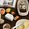 "Neutral tones with rustic textures; features a dark bread, yellow fruits, and earthy dishware against a wooden surface."