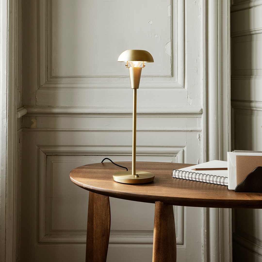 "Modern gold table lamp with a sleek design, set against a neutral-toned wooden table and soft wall backdrop."