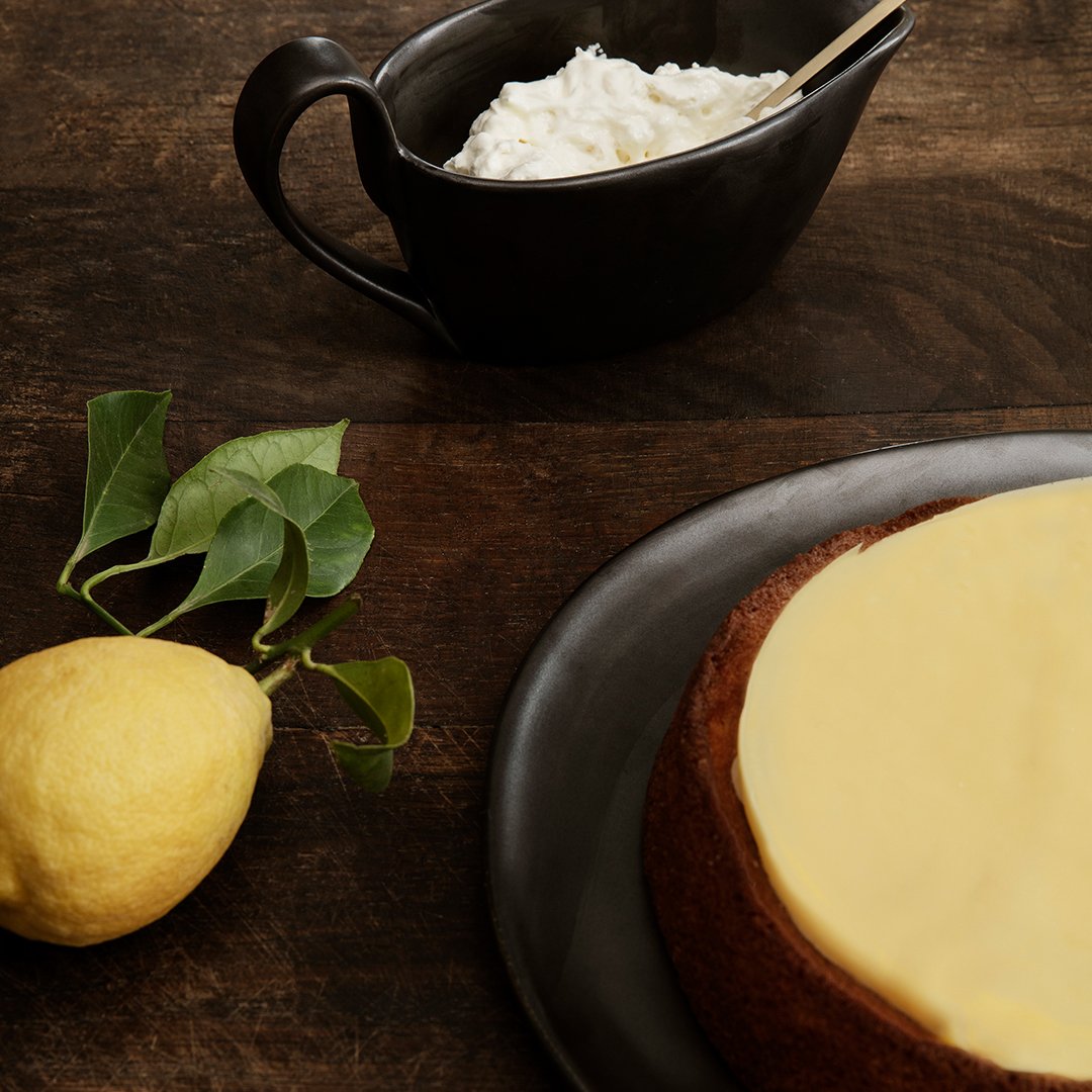 Yellow lemon, creamy white topping, dark brown plate, and black bowl on a rustic wooden surface.