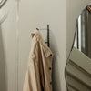 Beige trench coat hanging on a black hook against a neutral wall, with a modern mirror reflecting the space.