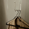 Beige shirt hanging on black hangers against a neutral wall background. Simple, stylish, and versatile design.