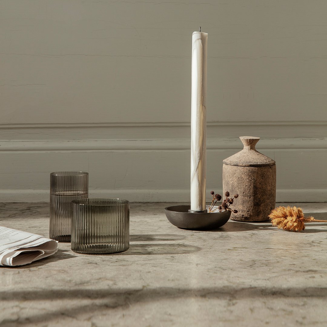 "Muted gray glassware with textured patterns, earthy tones in ceramics, and a white candle on a marble surface."
