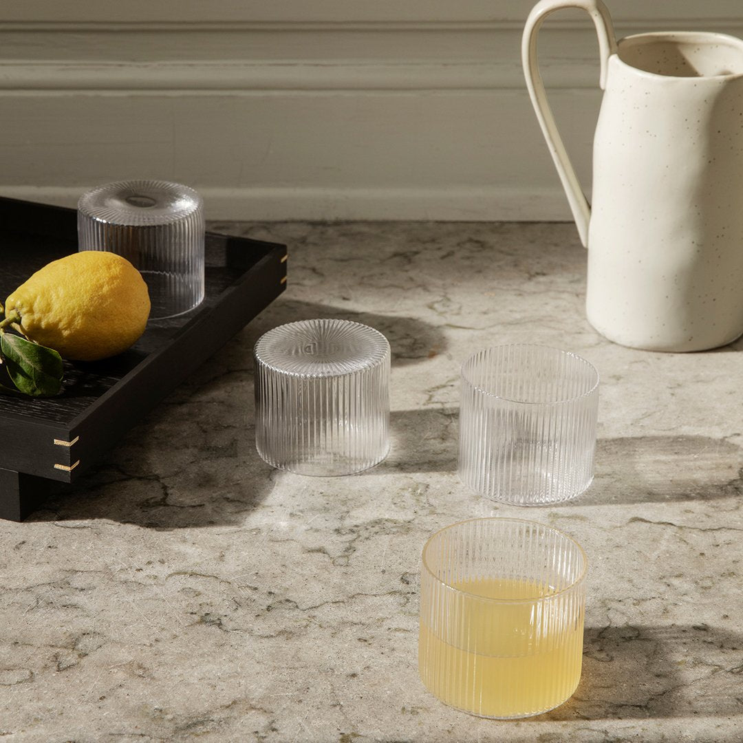 Clear and frosted ribbed glass cups on a marble surface, complemented by a lemon and a simple white pitcher.