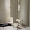 Beige two-step stool with smooth curves, set against a subtle gray wall and white flooring, creating a minimalist aesthetic.