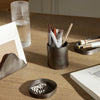 "Dark gray ceramic pencil holder with assorted pens and pencils on a wooden desk, surrounded by minimalist decor."