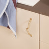 Elegant gold drawer handle on cream cabinet with soft blue and maroon linen towel draped nearby. Modern color palette.