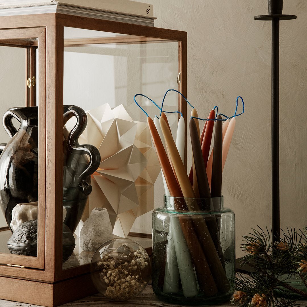 "Colorful tapered candles in a glass jar, showcasing warm tones of brown, cream, and teal against a neutral backdrop."