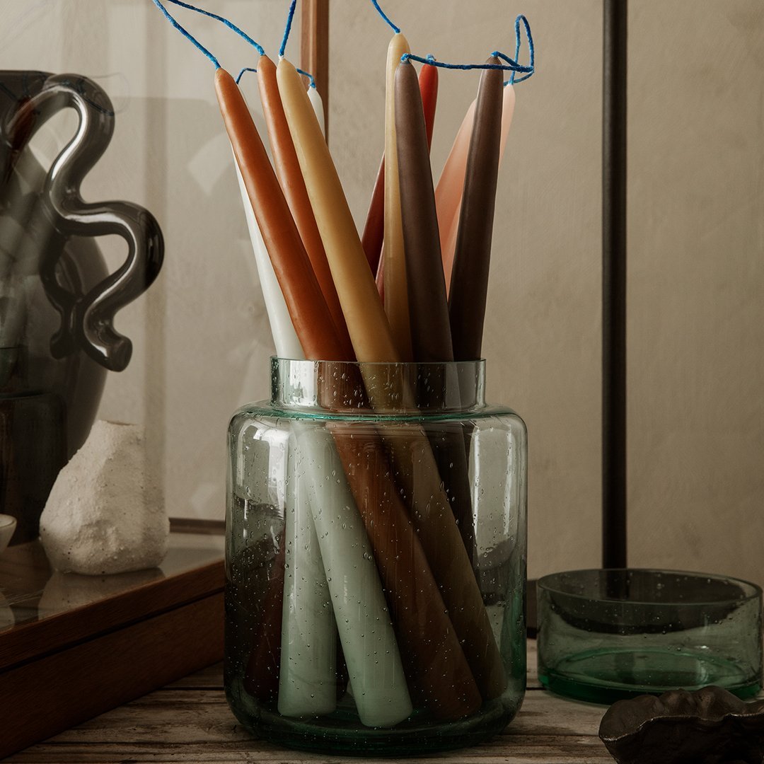 "Colorful tapered candles in various shades of orange, brown, green, and cream, displayed in a glass jar."