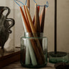 "Colorful tapered candles in various shades of orange, brown, green, and cream, displayed in a glass jar."