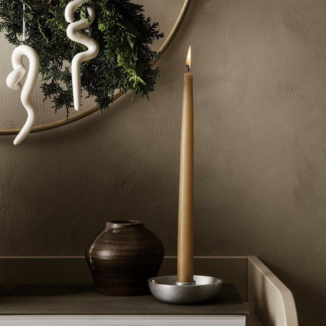 Tall amber candle in silver holder, dark ceramic vase, white decor accents, and rich earthy tones.