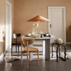 Modern dining room with a round gray table, wooden chairs, and a woven pendant light, featuring earthy tones and soft textures.