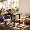 "Square wooden table with a dark frame, surrounded by light-colored chairs and vibrant striped cushions."