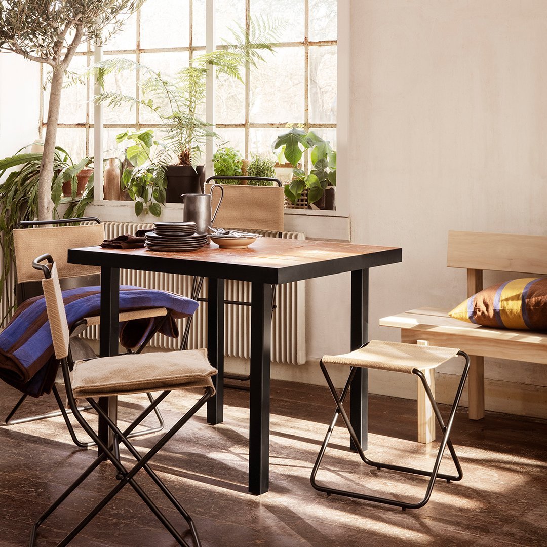 "Modern black and wood dining table with beige canvas chairs, accentuated by colorful striped cushions and greenery."
