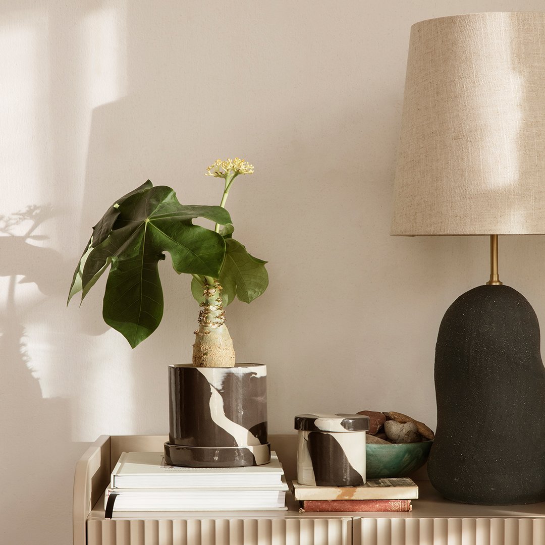 Black and white marble-patterned planter with a green plant, complemented by a neutral lamp and varying textures.