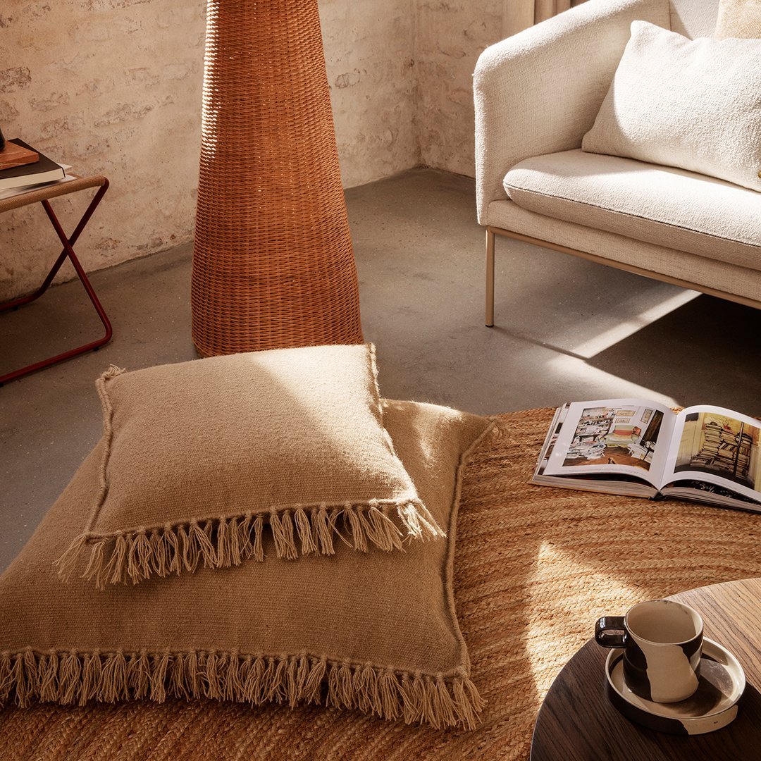 Two textured beige pillows with fringed edges, set against a natural, warm-toned living space.