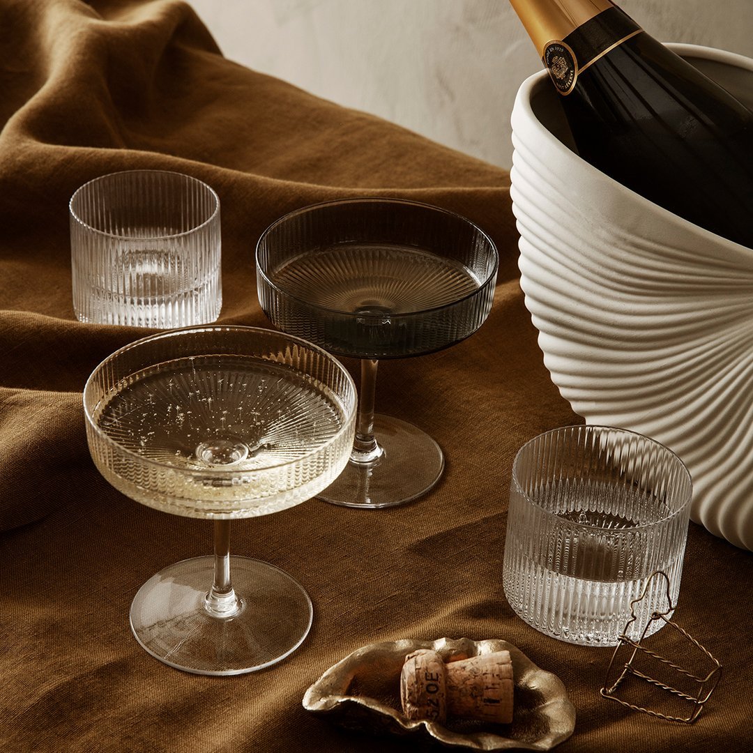 "Elegant glassware in clear, smoky black, and frosted finishes on a rich brown fabric backdrop."