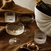 Elegant glassware set featuring clear, frosted, and black ribbed designs on a warm, textured brown tablecloth.