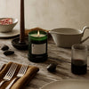 Green candle with geometric pattern, set on a rustic wooden table with neutral tones and textured glassware.