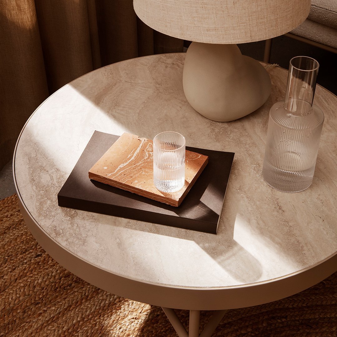 Light beige marble table with a dark wood tray and a warm-toned wooden book, complemented by neutral fabric and glass.