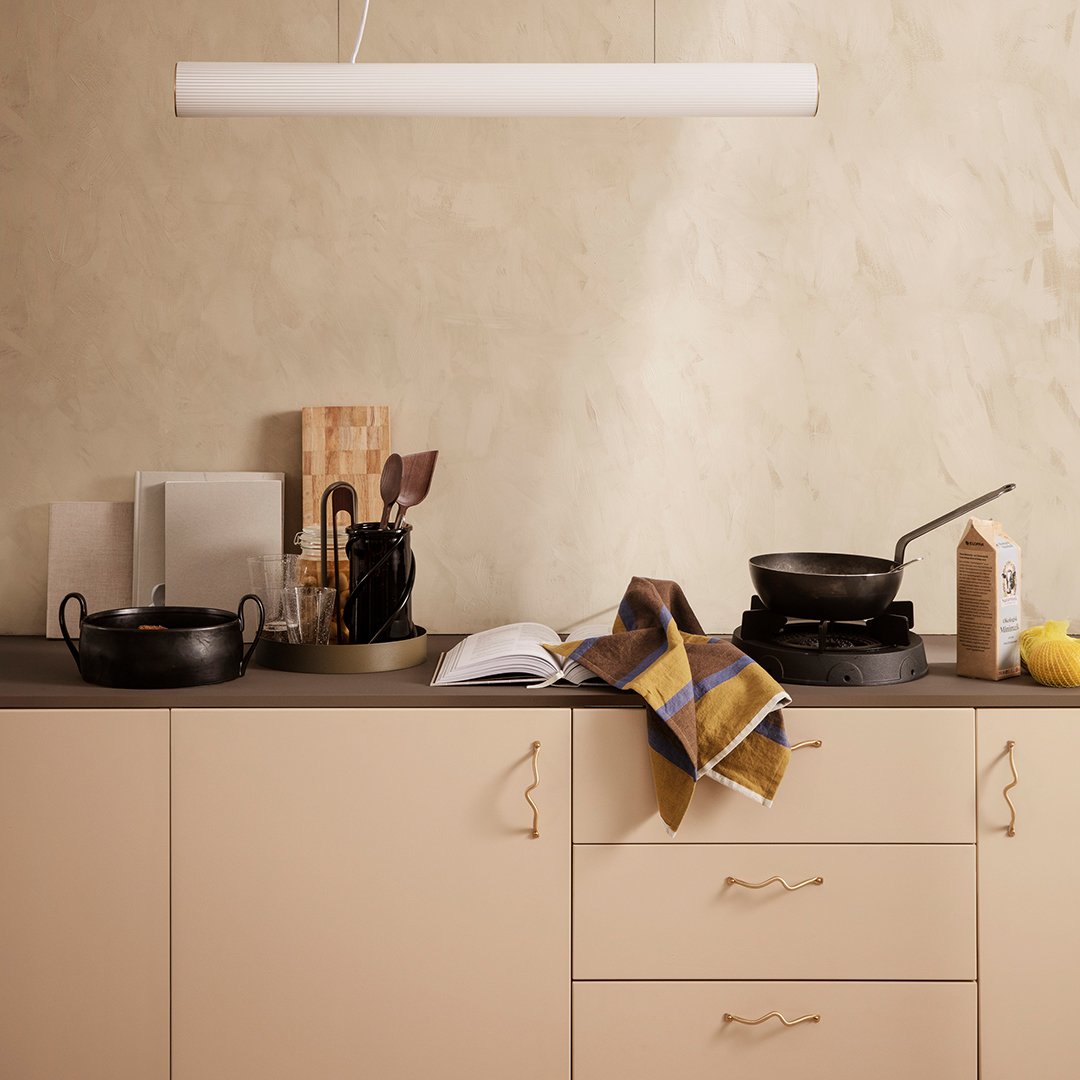 "Neutral beige cabinetry with black cookware and a patterned mustard, blue, and white kitchen towel draped on the counter."