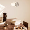 Modern pendant light in white and silver, hanging above a wooden table with neutral tones and minimalist decor.