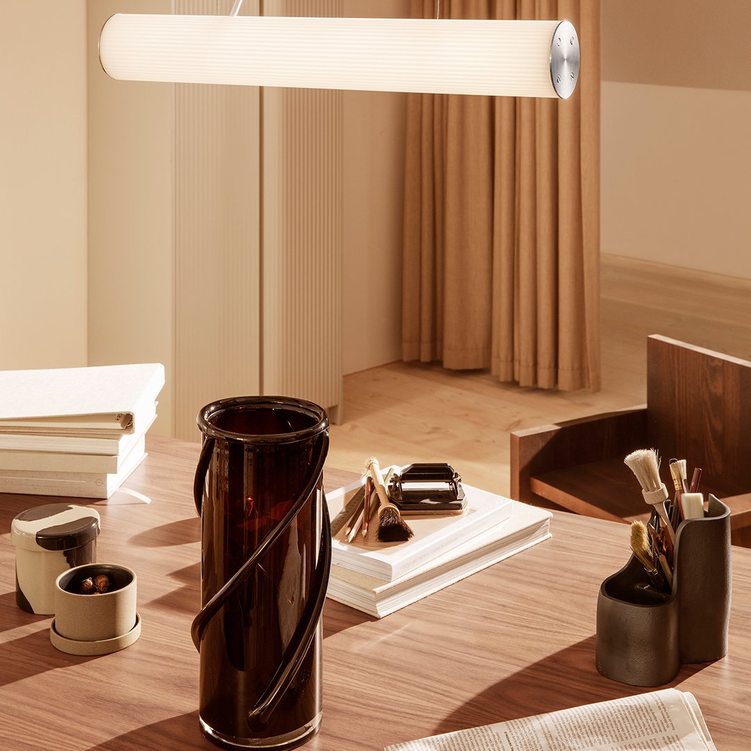 Modern, minimalist table lamp with a smooth white cylindrical shade; rich brown glass vase adds contrast to warm tones.